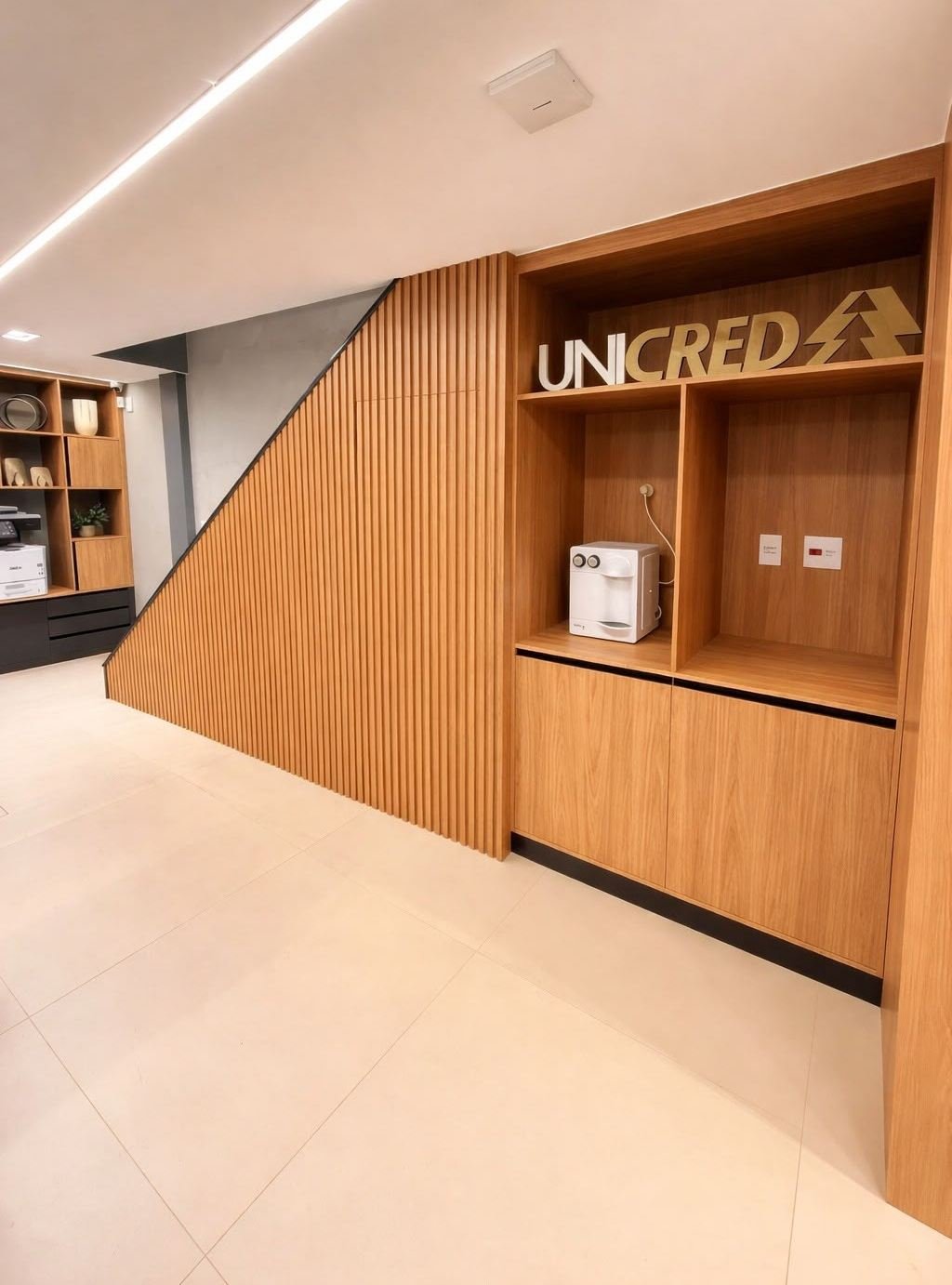 Recepção de agência com ripado acompanhando o vão da escada e nicho para o logotipo
