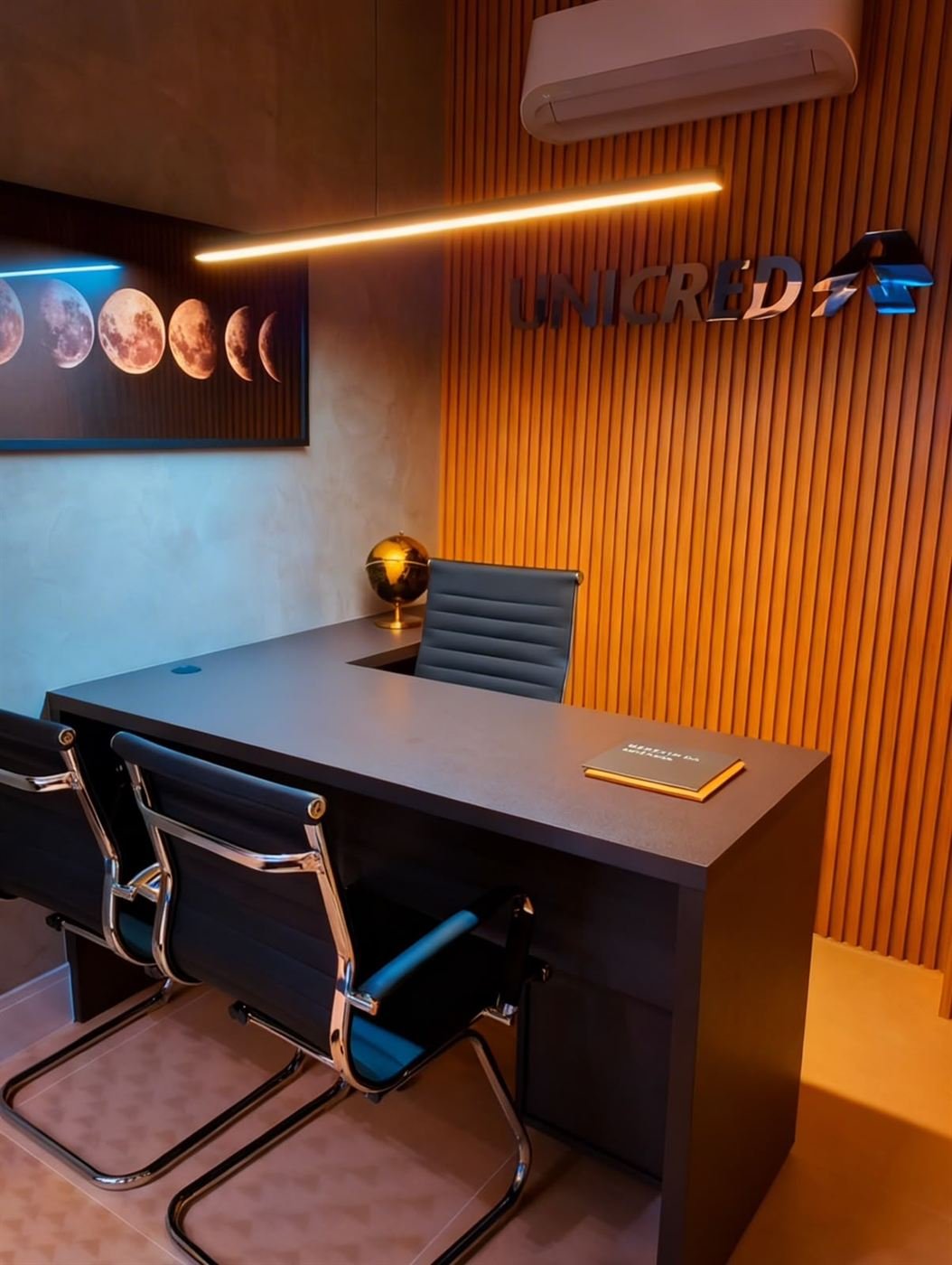 Sala de gerência de agência bancária com painel ripado, mesa em L e logotipo iluminado