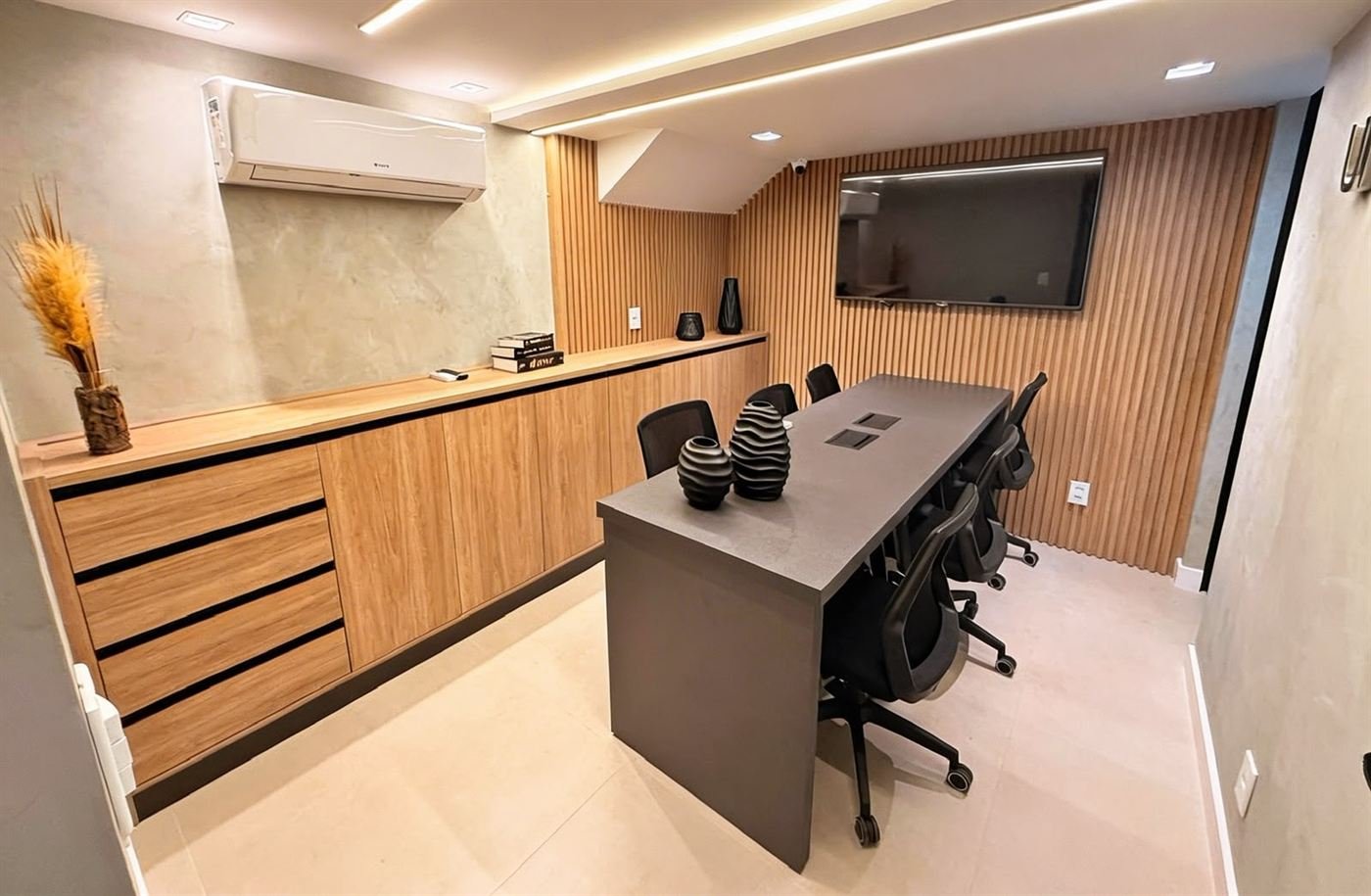 Sala de reunião com bancada amadeirada contínua e painel ripado atrás da TV